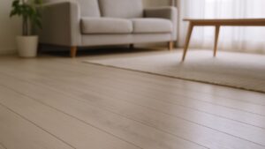 白い無垢材フローリングの上に、人の動線に沿った薄い黒ずみ。奥にソファとラグが見えるリビングの一角。