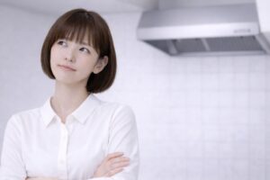 レンジフードを背景に、腕組みをして換気扇の掃除方法を考える女性